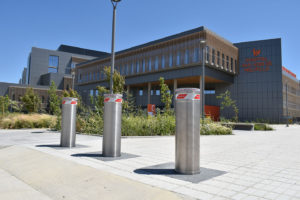Three Pilomat stainless steel automatic bollards installed in front of Hospital San José de Melipilla, with a modern building in the background.